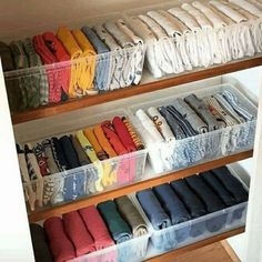 an organized closet filled with folded shirts and other items in plastic bins on wooden shelves