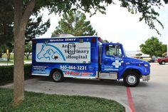 a veterinary hospital truck parked on the side of the road in front of a tree