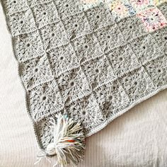 a crocheted blanket on top of a bed with a tasseled ball