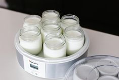 several jars filled with white candles sitting on top of a counter next to an empty container