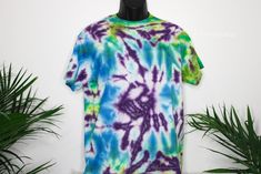 a tie - dyed shirt hanging on a wall next to plants