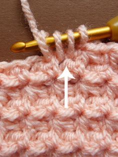 the crochet stitch is being worked on by a knitting needle with an arrow pointing at it