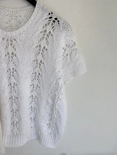 a white knitted sweater hanging on a clothes hanger next to a black and white wall