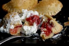 a piece of pie with whipped cream and strawberry filling on a black plate next to a fork