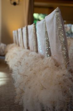 there is a row of chairs that have white feathers on them and are lined up with silver sequins