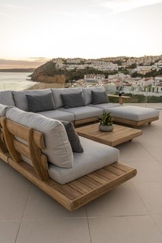 a couch and table sitting on top of a patio next to the ocean with buildings in the background