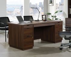 an office desk with two laptops on it in front of a large window overlooking the city