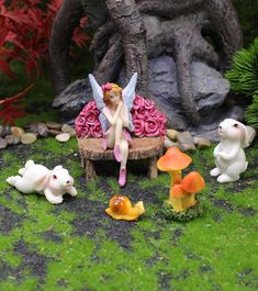 a fairy garden with figurines sitting on a bench surrounded by flowers and mushrooms