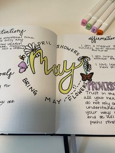 an open notebook with writing on it and some colored markers next to the book that says may