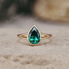 a gold ring with an emerald colored stone in the center on a marble table top