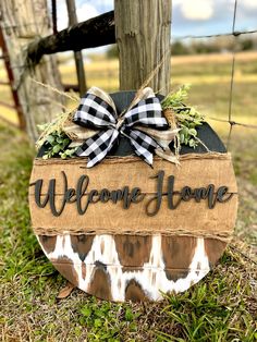 a welcome home sign with a bow on it sitting in the grass near a fence