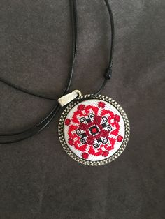 a red and white cross stitched pendant on a black cord with a silver clasp