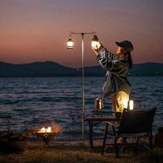 a woman standing on top of a beach next to the ocean holding a lantern in her hand