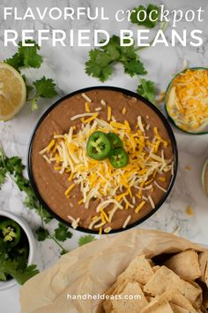 a bowl filled with cheese and green peppers next to tortilla chips