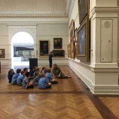 a group of children sitting on the floor in front of an older man talking to them