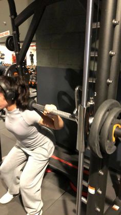 a woman is doing squats in the gym with headphones on and holding a barbell