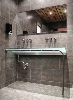 a bathroom with grey tiles and a mirror on the wall above it is a sink