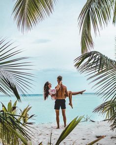 a man carrying a woman on his back while standing in front of palm trees at the beach