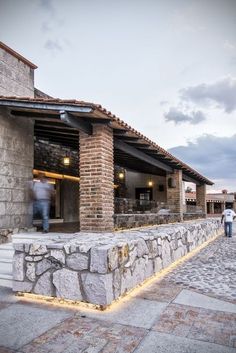 two people are walking past a building with stone walls and steps that lead to the entrance