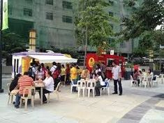 many people are sitting at tables in the middle of an open air area with food trucks behind them