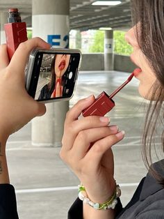 a woman taking a selfie with her cell phone and lipstick in the other hand