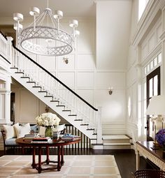 an elegant staircase with chandelier and flowers in vases on the end table