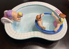 two figurines in the shape of people swimming in a pool on top of a table