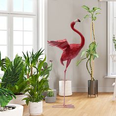 a pink flamingo standing in the middle of a living room with potted plants