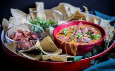 a red bowl filled with tortilla chips next to salsa and guacamole