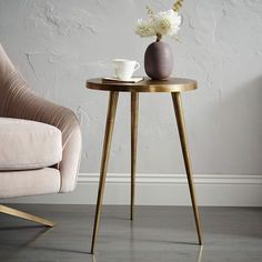 a small table with a vase on it next to a chair and a wall behind it