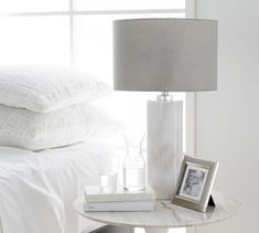 a table with a lamp and some books on it next to a bed in a bedroom