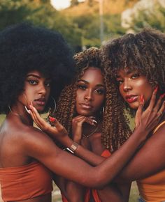 three young women with afro hair posing for the camera, one holding her hands on her chest