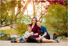 a woman, man and child sitting on the ground in front of some trees at sunset