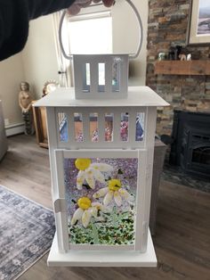 a person holding a white lantern with yellow flowers on it in front of a fireplace