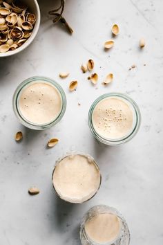 two glasses filled with peanut milk next to some nuts