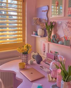 a pink desk topped with a laptop computer sitting next to a vase filled with flowers