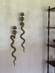 two metal candlesticks sitting next to each other in front of a white wall