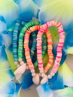 three bracelets with beads and pearls are on top of a blue flower petals background