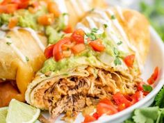 two burritos on a plate with guacamole and tomatoes