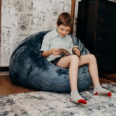 a young boy sitting on a bean bag chair reading a book while wearing slippers