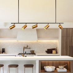 a kitchen with white counter tops and gold lights hanging from the ceiling over the island