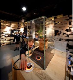 children looking at an object in a glass case with light coming from the top and hands on it