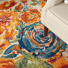 an orange and blue floral rug in a living room with a white chair next to it