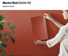 a woman holding a piece of red paper next to a plant