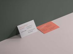 two business cards sitting next to each other on top of a white table with green and gray walls