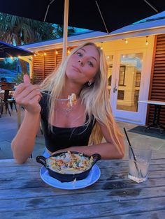 a woman sitting at an outdoor table with food in front of her and eating from a bowl