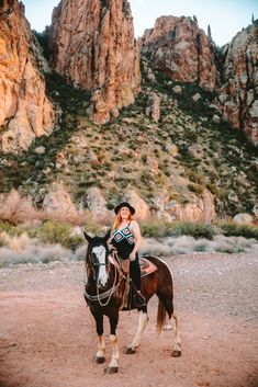 a woman riding on the back of a brown and black horse in front of mountains