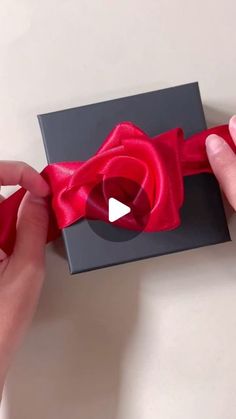 a person is opening a gift box with a red ribbon on it and another hand holding the bow