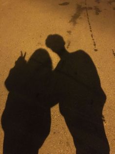 two people standing next to each other with their shadows on the ground in front of them