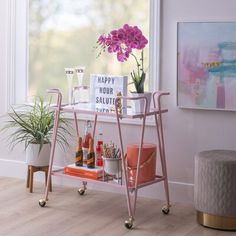 a pink bar cart with bottles and drinks on it in front of a large window